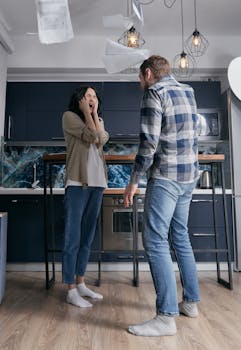 A couple arguing in a modern kitchen, surrounded by flying papers. Emotionally tense moment.