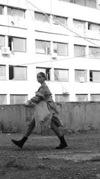 Black and white photo of a fashionable woman walking briskly on a city rooftop.